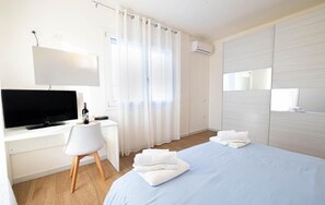 Hotellihuone, jossa on sänky, työpöytä, jossa on televisio, tuoli ja ikkuna, jossa on verhot.