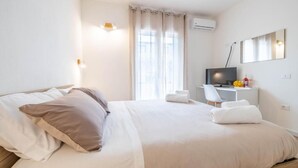 Una camera d'albergo con un letto, una scrivania con un computer, una televisione e una finestra con tende.
