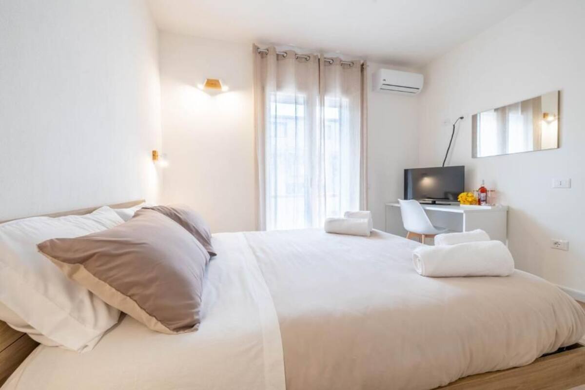 Ein Hotelzimmer mit Bett, Schreibtisch mit Computer, Fernseher und einem Fenster mit Vorhängen.