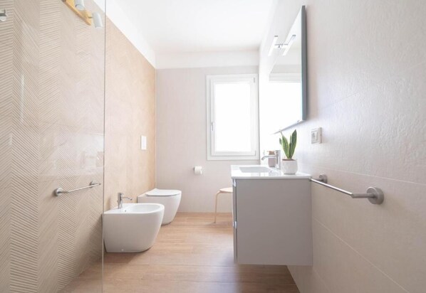 A modern bathroom with a shower, toilet, and sink, featuring a herringbone-patterned wall and a potted plant. - Corona Guest House (Sestu)