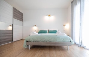 A modern bedroom with a bed, bedside lamps, and a view of the outside.