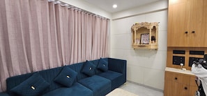 A room with a blue sofa, a wooden cabinet, and a wall-mounted shelf with a framed picture.