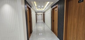 A hotel hallway with a polished marble floor, wooden doors, and a ceiling with recessed lighting. - Hotel Silvera Inn (Ahmedabad)