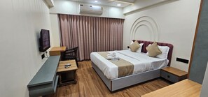 A hotel room with a bed, bedside tables, a desk, a chair, an air conditioner, and a TV.