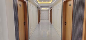 Un couloir d’hôtel avec des portes en bois, des panneaux indiquant le numéro des chambres et un sol carrelé.