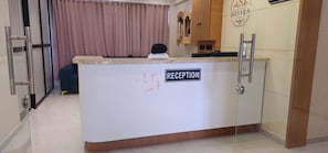 A reception desk with a sign, a person seated behind it, and a curtain in the background. - Hotel Silvera Inn (Ahmedabad)