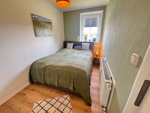 Ein Schlafzimmer mit Bett, Heizkörper, Fenster und einem Bild an der Wand.