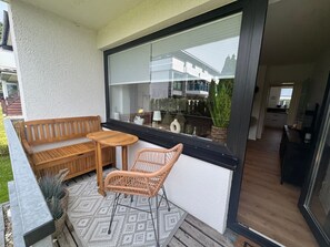 Ein Balkon mit einer Holzbank, einem Korbstuhl und einem kleinen Tisch.
