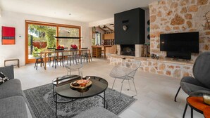 Un amplio salón con comedor, chimenea y televisor montado en una pared de piedra.