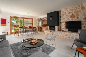 A spacious living area with a dining set, a fireplace, and a TV mounted on a stone wall.