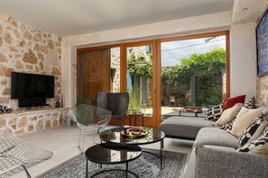 A living room with stone walls, a flat-screen TV, a sofa, a coffee table, and a chair. - Villa Maxima Agri (100641-K1) - Filipini (Filipini)