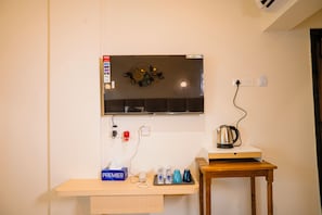 A room with a wooden desk, a small table, a kettle, a phone, and a Premier box. - Breeze Inn Beach Resort (Shrivardhan)
