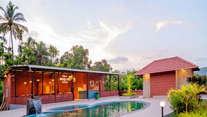 A poolside area with a bar, a small building with a red roof, and a waterfall feature. - Breeze Inn Beach Resort (Shrivardhan)