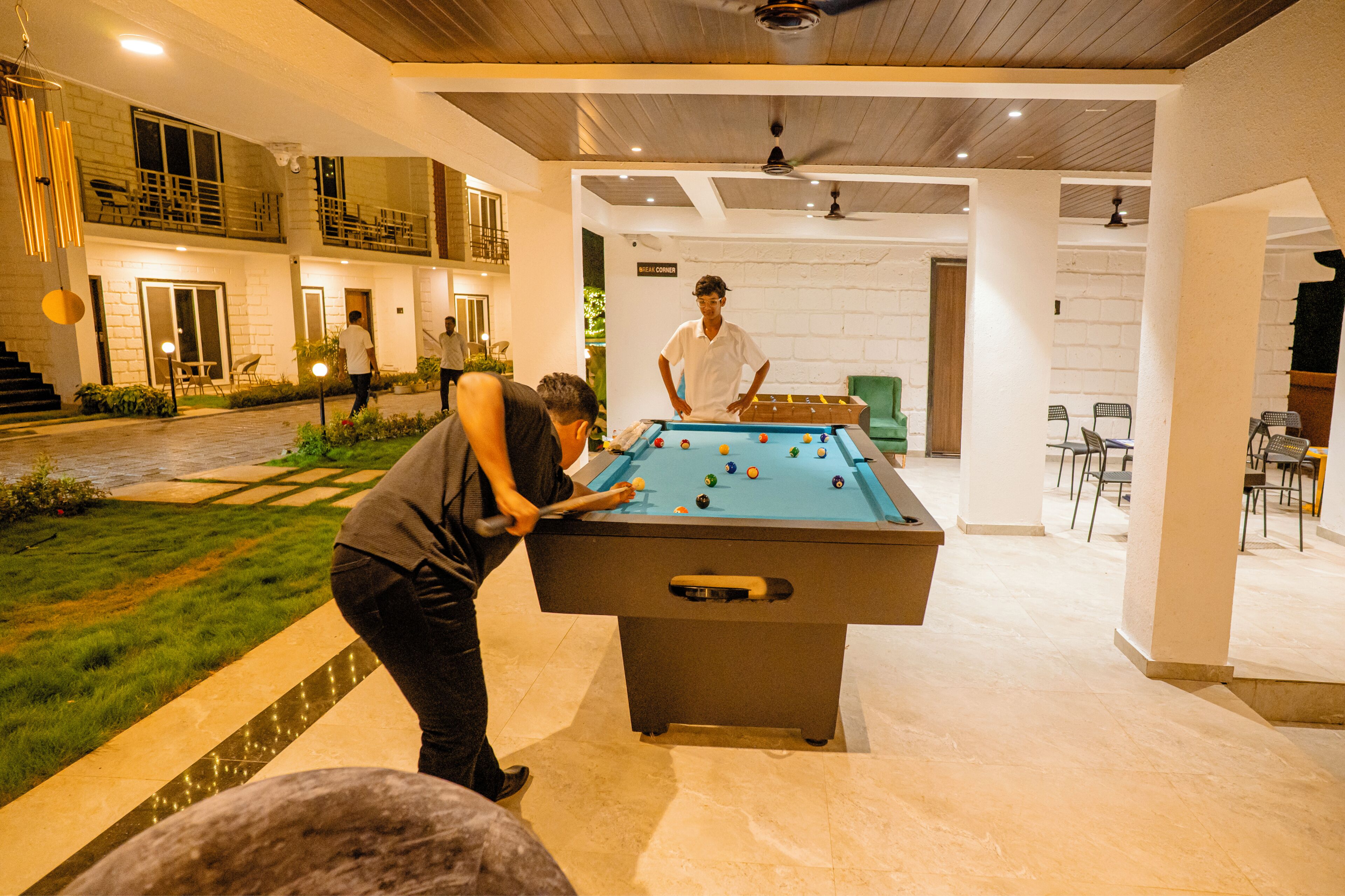 A pool table in a well-lit indoor space with a stone wall and a balcony.
