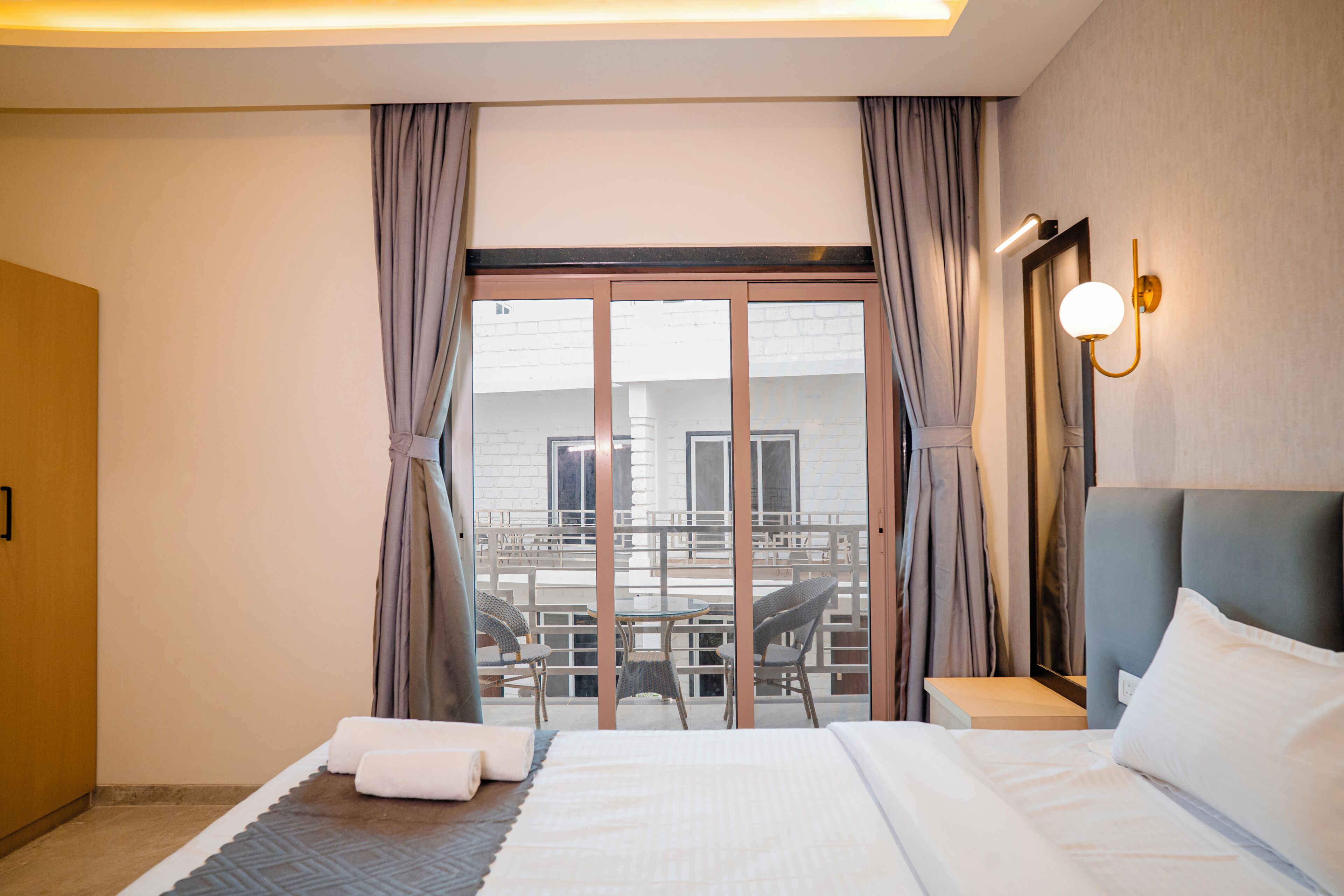 Habitación de hotel con cama, una mesita, una silla y vistas a un balcón con mobiliario exterior.