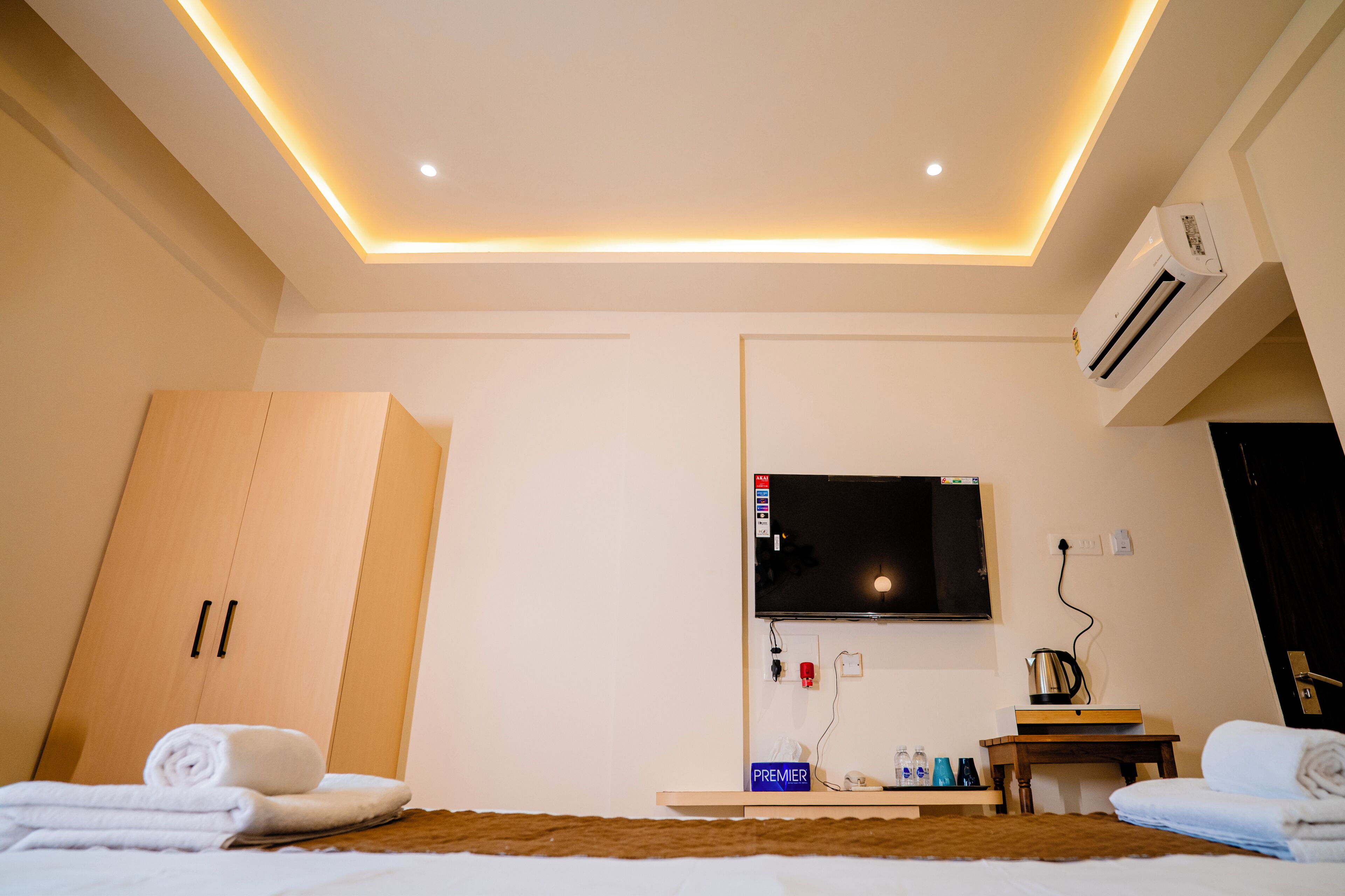 A hotel room with a bed, a TV mounted on the wall, an air conditioning unit, and a wooden wardrobe.
