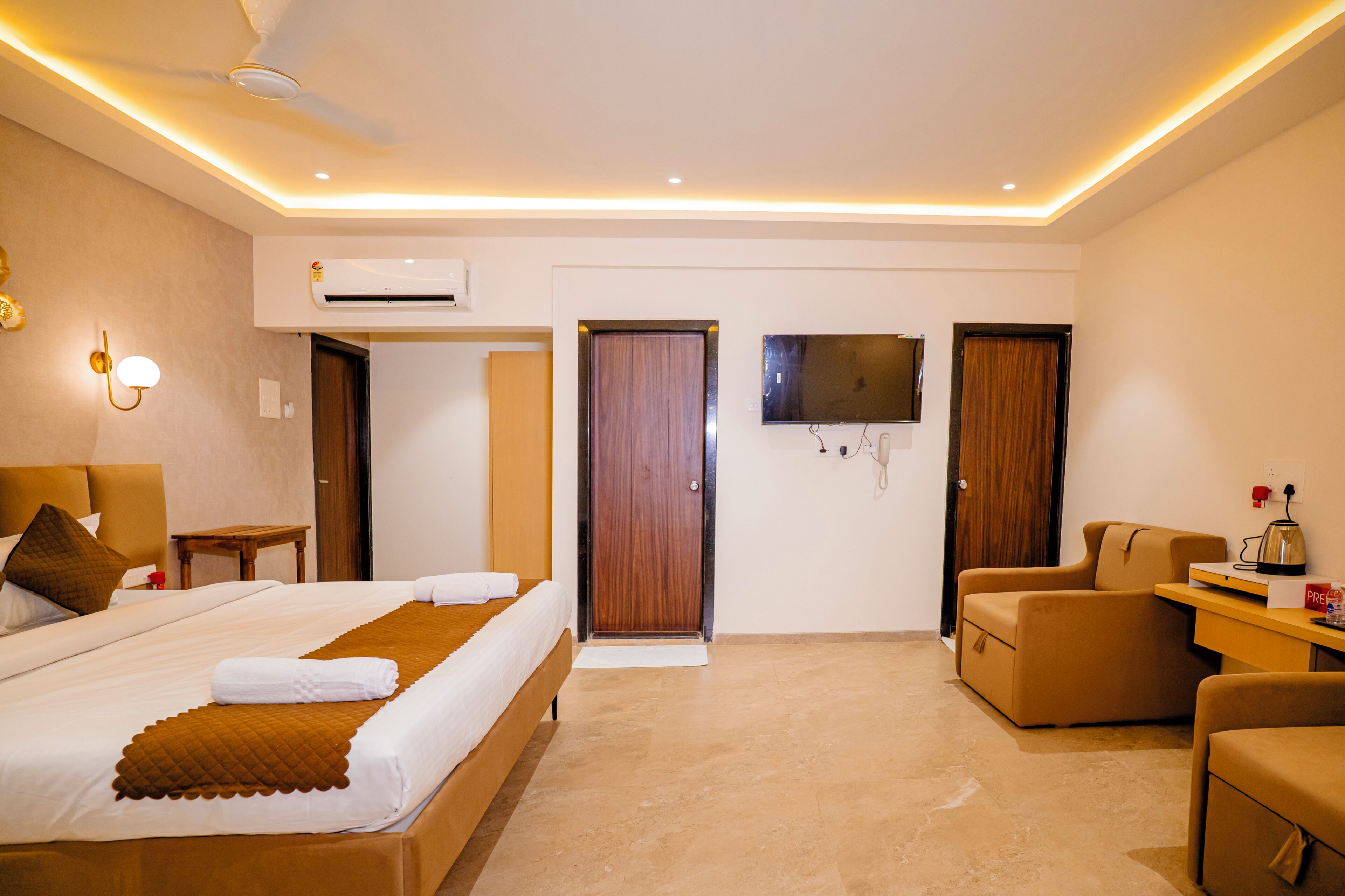 A hotel room with a bed, a desk, a chair, a TV, and an air conditioning unit.