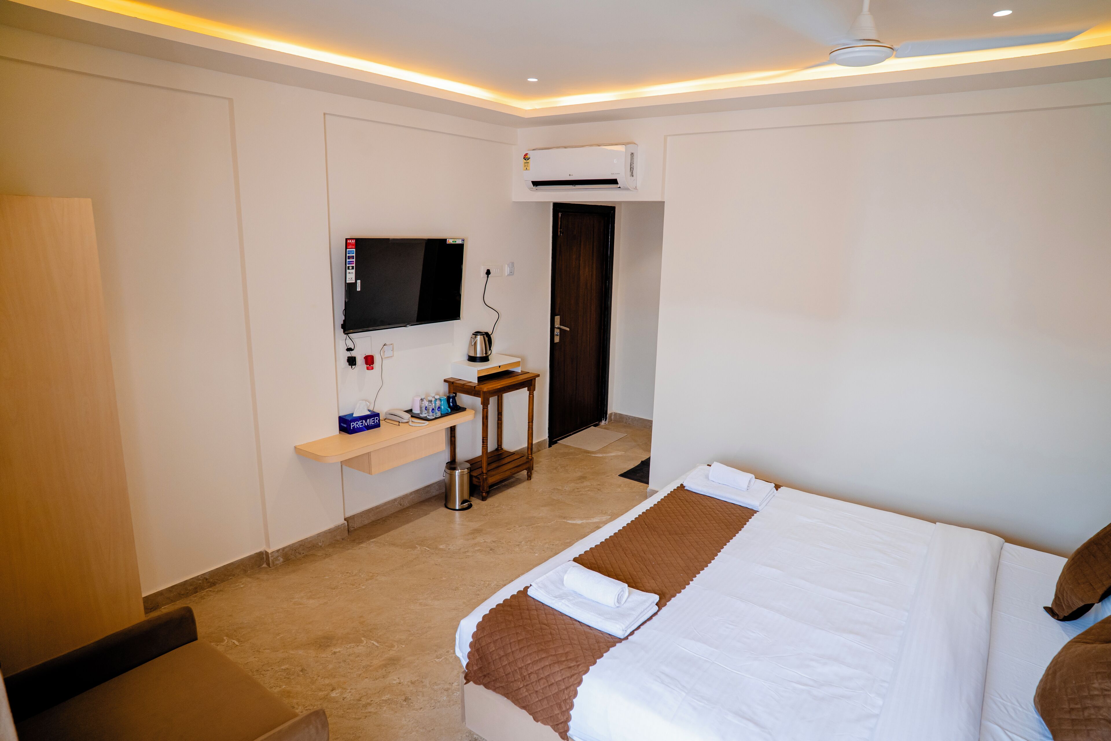 Habitación de hotel con una cama, televisión, equipo de aire acondicionado, una mesita con tetera y una puerta.