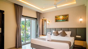 A modern hotel room with a large bed, a ceiling fan, a painting, and a view through the glass door. - Breeze Inn Beach Resort (Shrivardhan)