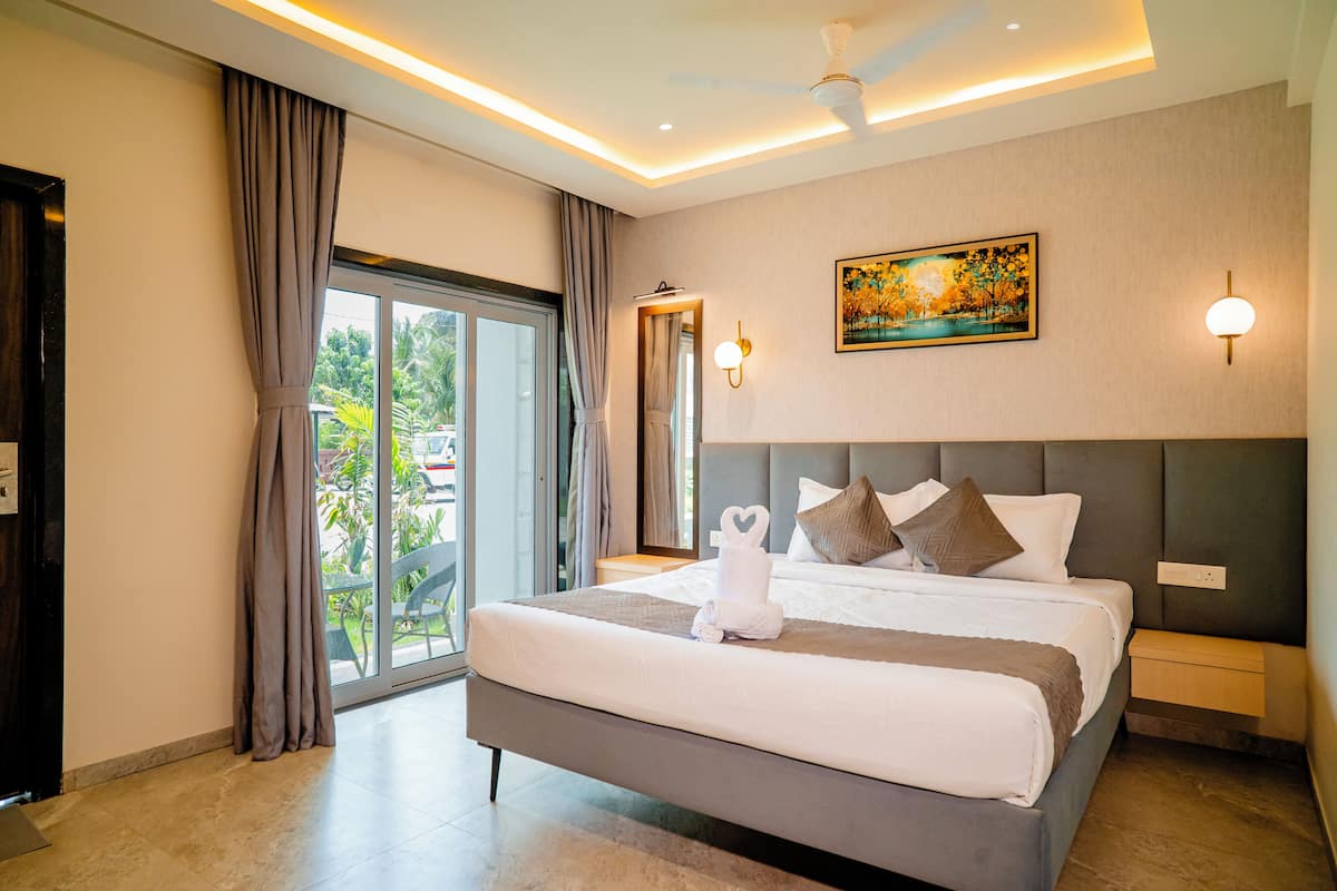 A modern hotel room with a large bed, a ceiling fan, a painting, and a view through the glass door.