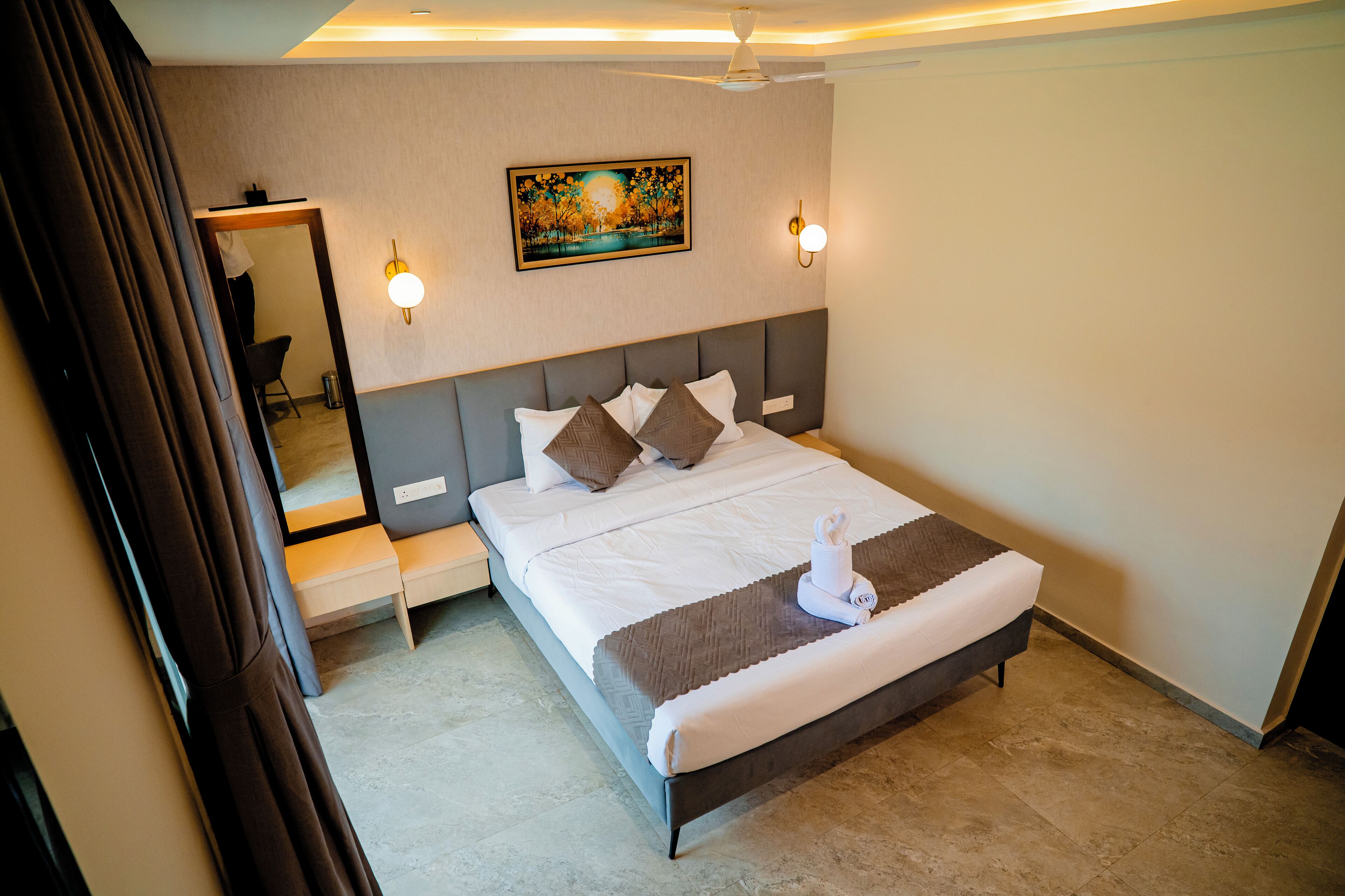 A hotel room with a bed, bedside table, wall-mounted artwork, and a ceiling fan.