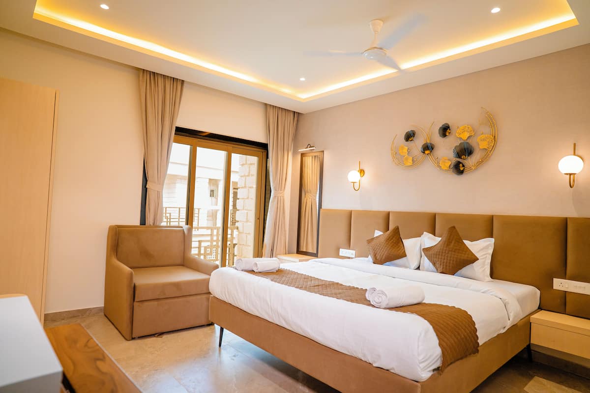 A hotel room with a bed, a chair, a bedside table, a wall-mounted light fixture, and a ceiling fan.