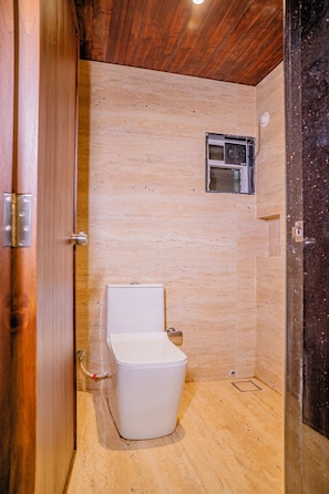 A small, enclosed bathroom with a wooden ceiling, a white toilet, and a small window. - Breeze Inn Beach Resort (Shrivardhan)