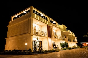 A multi-story building with balconies, a well-lit entrance, and a paved driveway. - Breeze Inn Beach Resort (Shrivardhan)