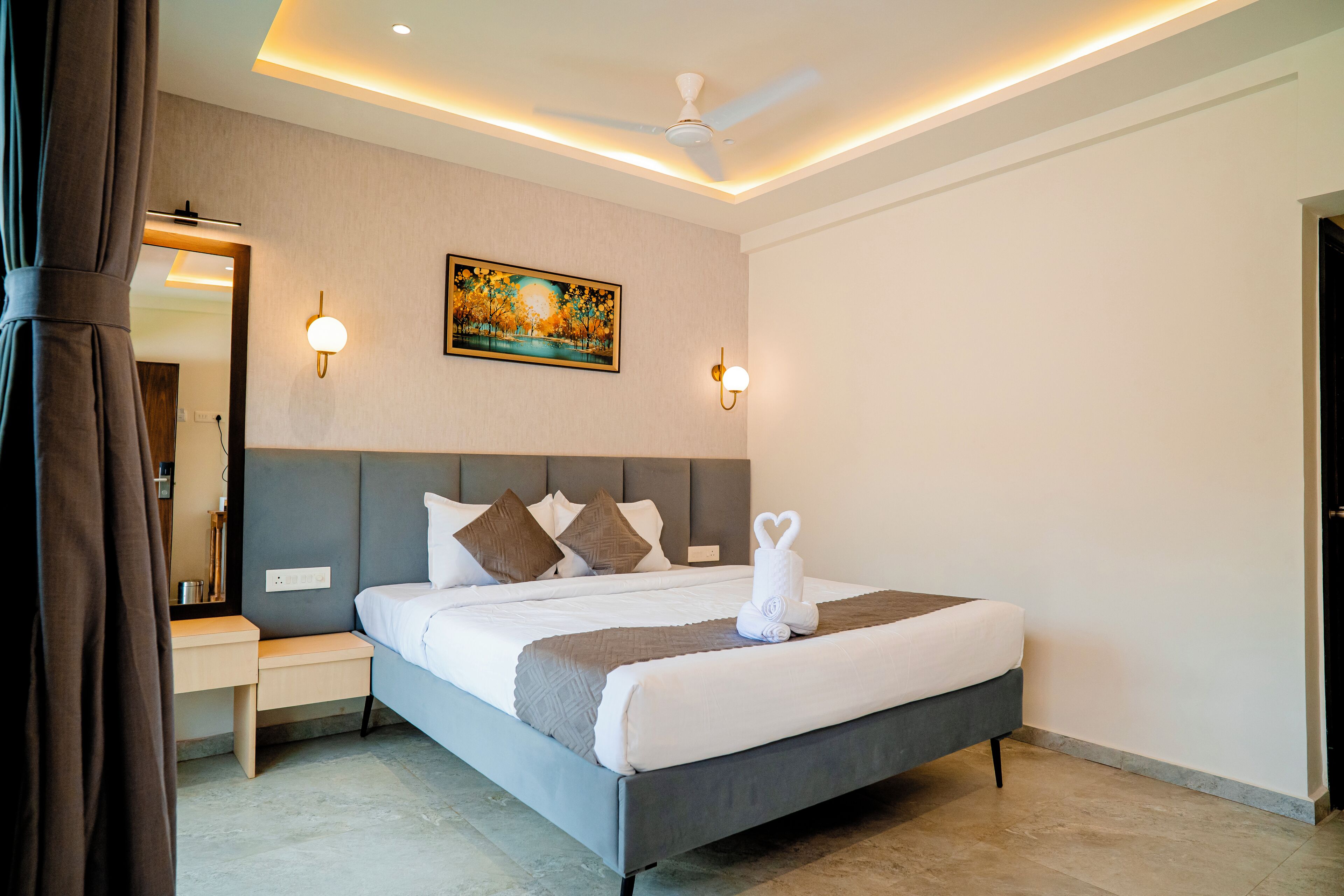 Een moderne hotelkamer met een groot bed, nachtkastje, wanddecoratie, plafondventilator en sfeerverlichting.