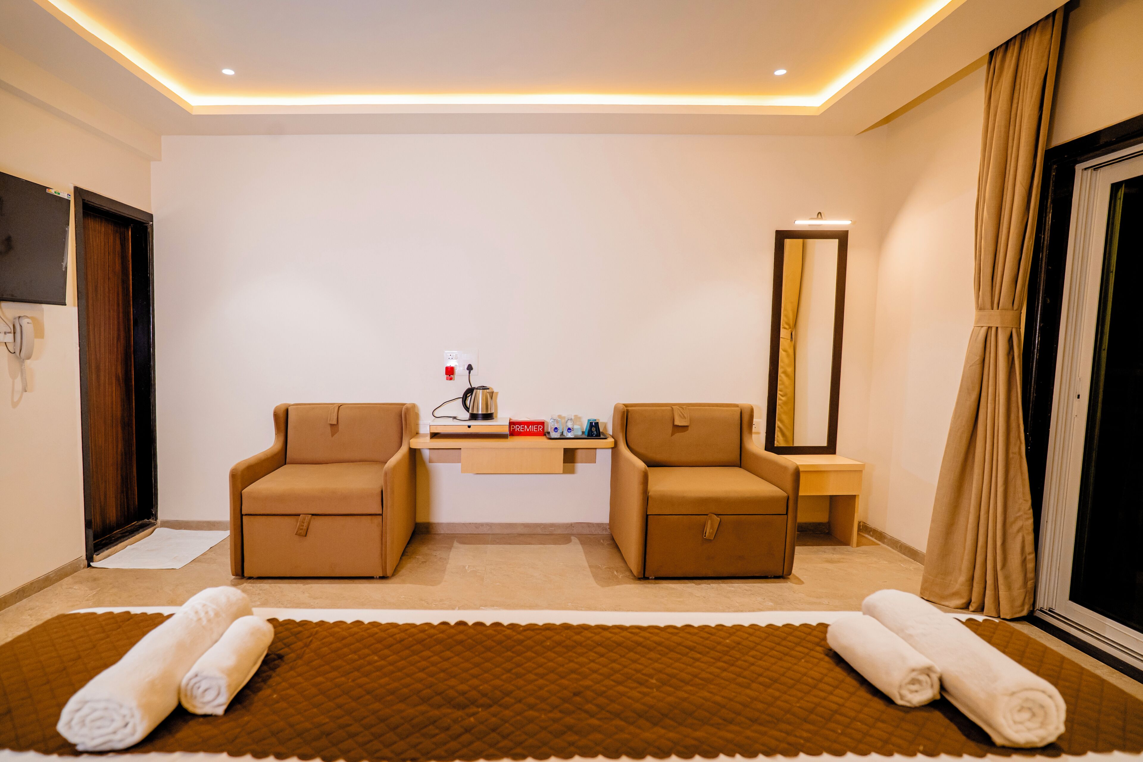 Habitación de hotel con dos sofás, una mesita de noche, un espejo y una cama grande con alfombra marrón.