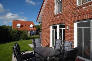 Een bakstenen huis met een patio tafel en stoelen, een schuifdeur en een omliggend huis met een rood dak.