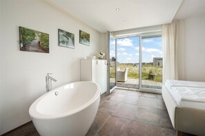 Een moderne badkamer met een vrijstaand bad, een douchegedeelte met glazen wanden en een bed met uitzicht op het omliggende landschap.