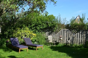 Ein Garten mit zwei Liegestühlen, einem Holzzaun und einem Gebäude im Hintergrund.