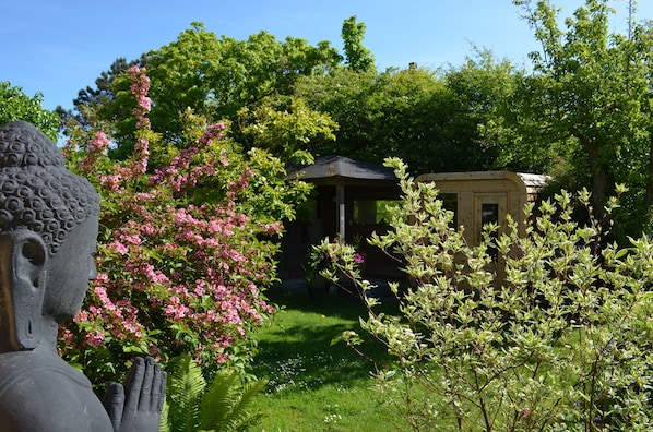 Un jardin agrémenté d’une statue de Bouddha, d’un belvédère et d’une végétation luxuriante.