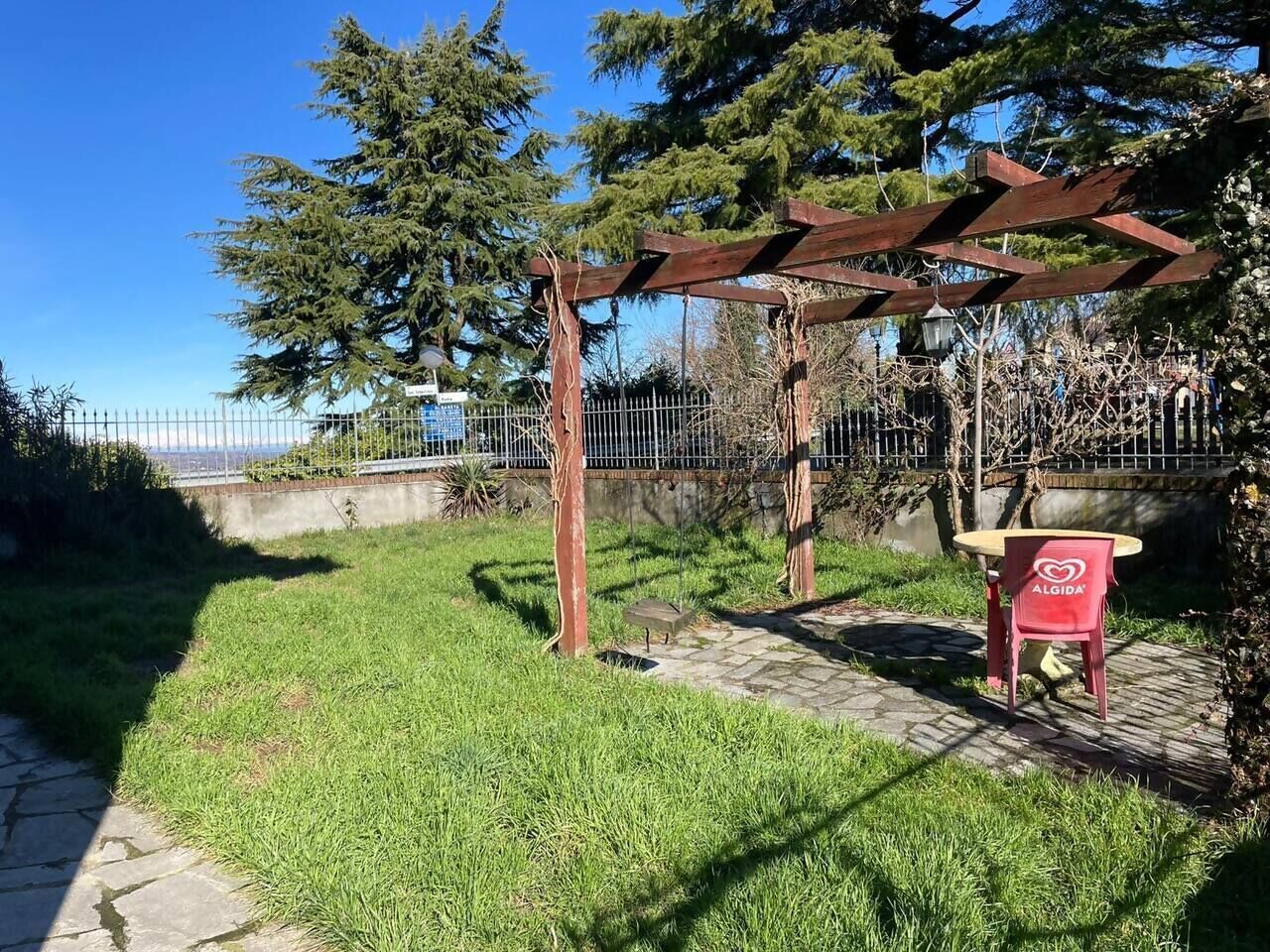 A garden area with a pergola, a red chair, and a stone pathway.