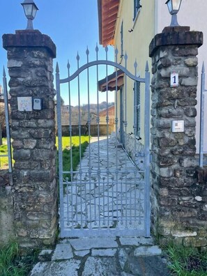 A gated entrance with stone pillars, a metal gate, and a house with a red roof.