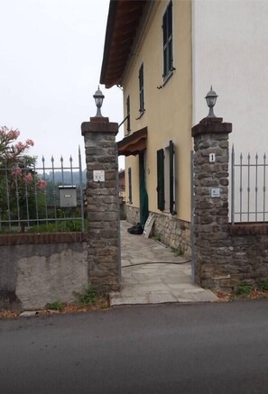 A building with a stone gate, a paved entrance, and a metal fence.