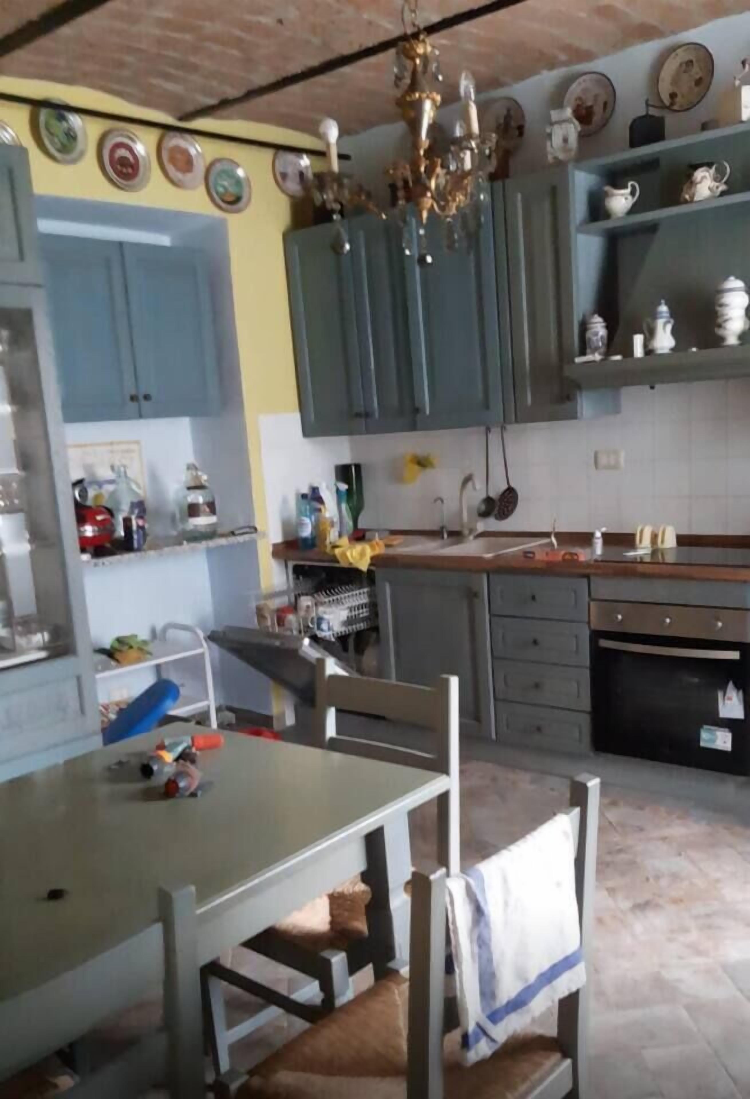 Una cocina con armarios grises, una mesa de comedor, sillas y una araña.