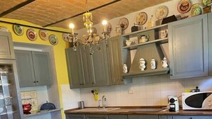 A kitchen with grey cabinets, a dining table with chairs, a chandelier, and a microwave. - Villetta in collina in Piemonte (Morsasco)