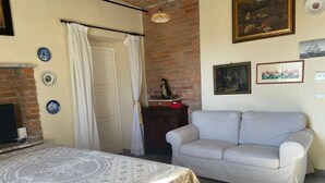 A room with a bed, a sofa, a brick wall, a fireplace, and a ceiling light. - Villetta in collina in Piemonte (Morsasco)