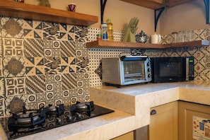 A kitchen with patterned tiles, a gas stove, a toaster, and a microwave. - Aliya Villa by Betterplace (Seminyak)
