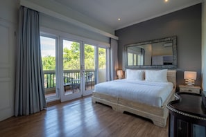 A bedroom with a large bed, a mirror, a nightstand, and a view through a sliding glass door. - Aliya Villa by Betterplace (Seminyak)