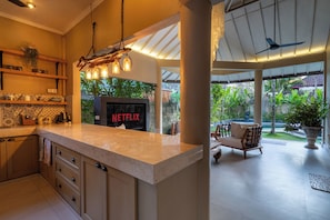 A kitchen with a large island, a Netflix sign, and a view of the garden. - Aliya Villa by Betterplace (Seminyak)