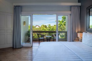 A hotel room with a large bed, a balcony with chairs, and a view of greenery. - Aliya Villa by Betterplace (Seminyak)