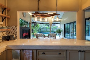 A modern kitchen with a large island, a hanging light fixture, and a view of the outdoor patio area. - Aliya Villa by Betterplace (Seminyak)