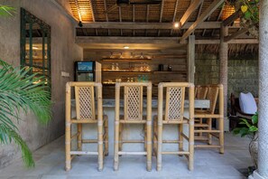 A bar area with bamboo chairs, a counter with glassware, and a thatched roof ceiling. - Aliya Villa by Betterplace (Seminyak)