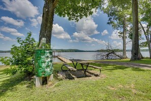 En picknickplats vid sjön med en bänk, ett picknickbord och en grön soptunna.