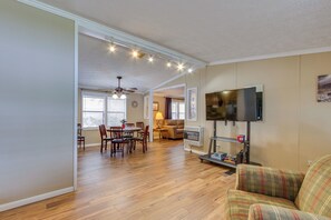 A living room with a television, a dining area with a table and chairs, and a kitchen area with a refrigerator.