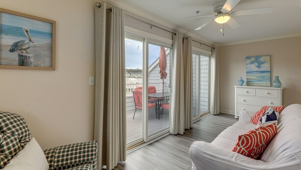 Een kamer met een bed, een geruit stoel, een witte kaptafel en een schilderij van een pelikaan.