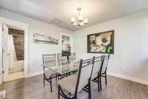 A dining area with a glass table and chairs, a chandelier, and artwork on the walls.